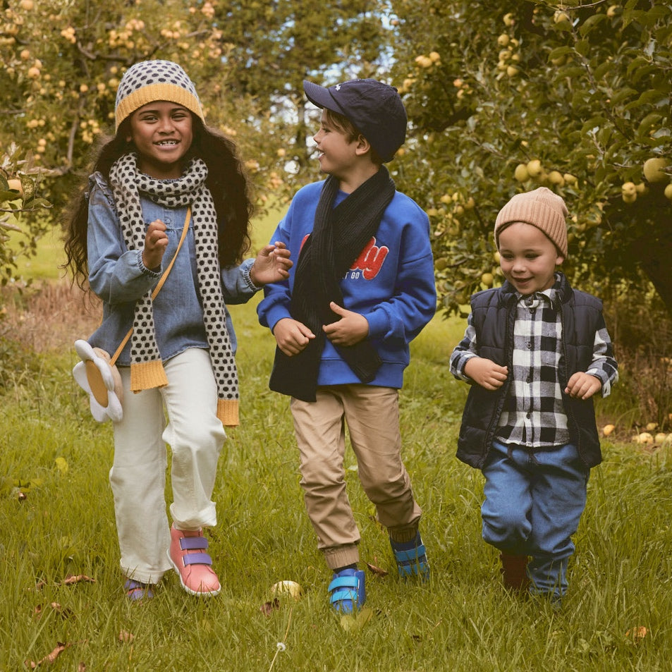 three kids in an autumnal orchard, wearing bobux trainers