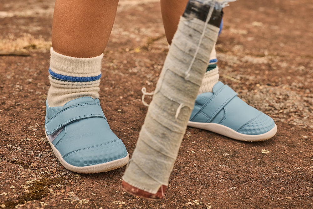 Image of a pair of children's feet wearing light blue Bobux shoes with velcro straps