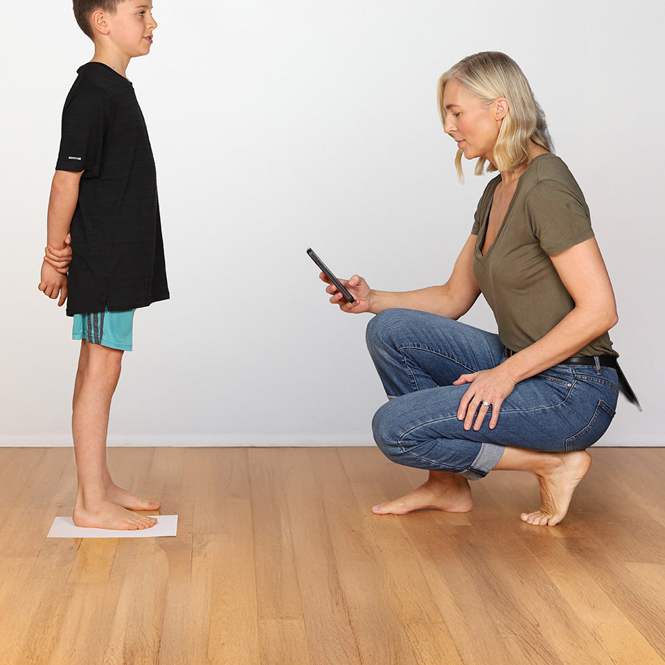 Photograph of a mother photographing her sons feet while he stands on a sheet of paper