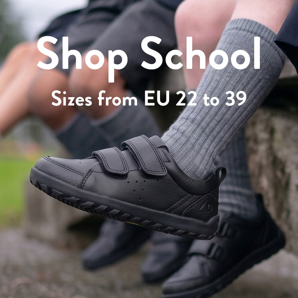 Children's feet wearing black school shoes with socks. Large white text across the centre reads 'Shop School - sizes from EU 22 to 39'.
