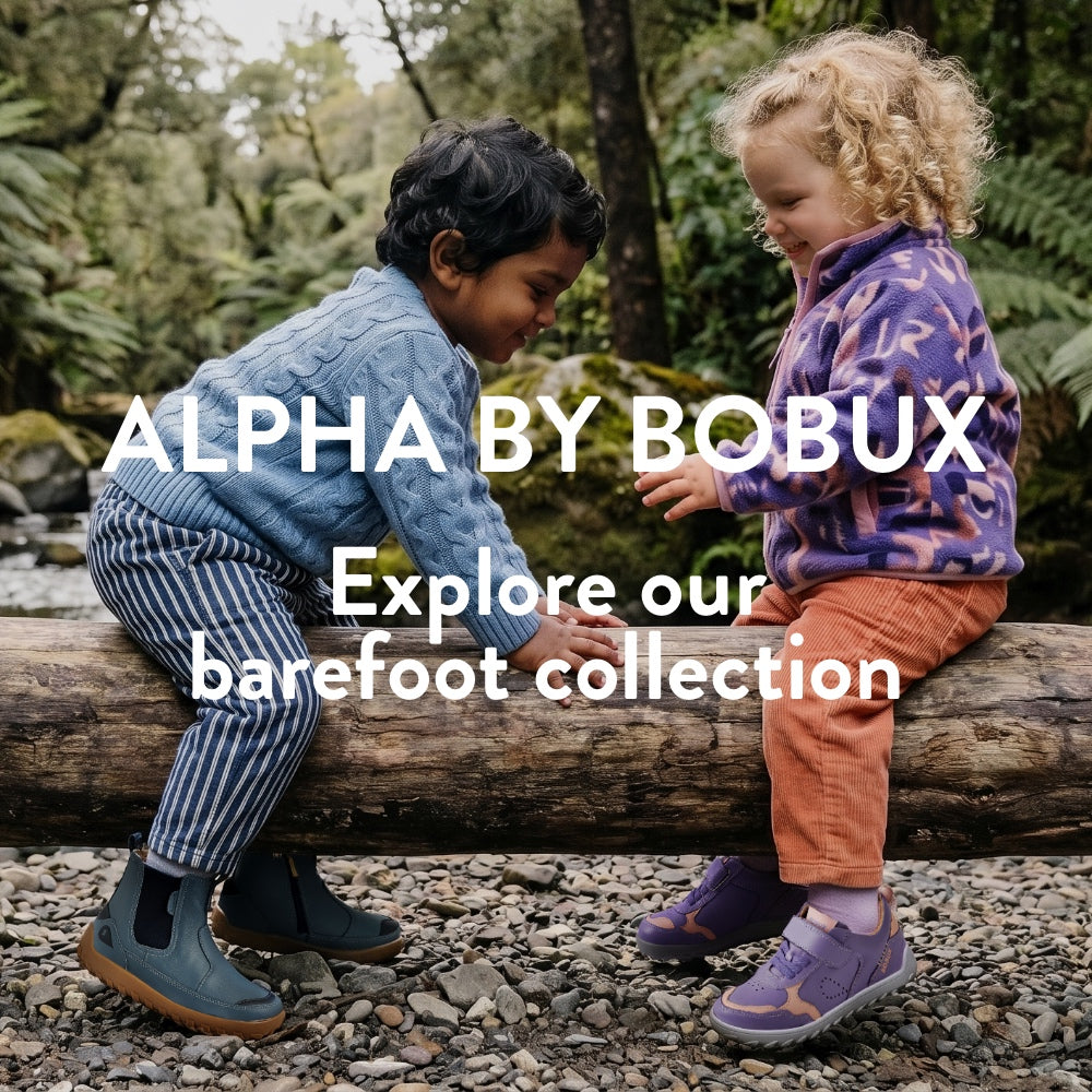 children playing on a log in a forest, both wearing bobux barefoot style shoes