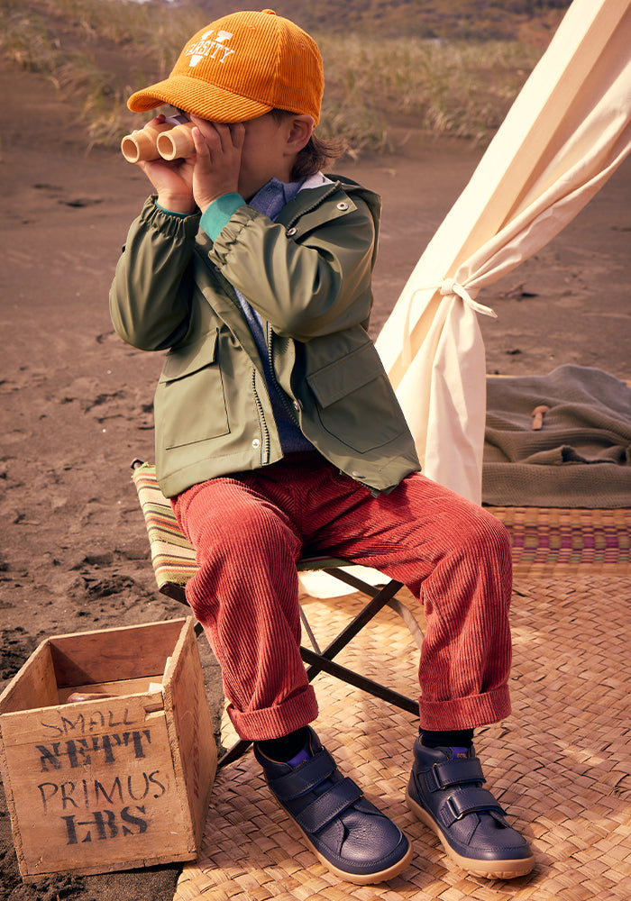 Image of a boy with binoculars on an autumn beach wearing Bobux boots