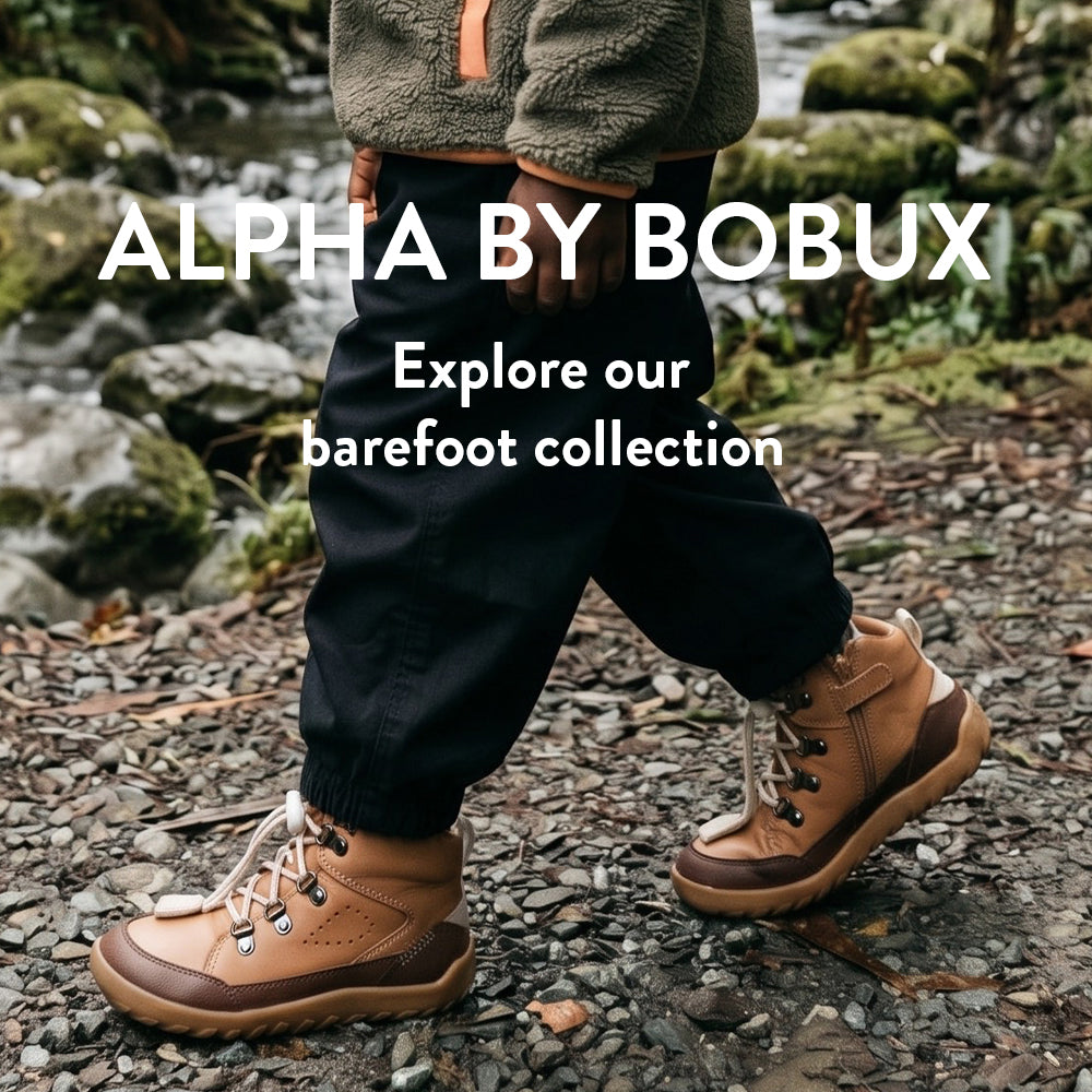 A child outdoors near a stream wearing tan lace-up barefoot-style boots. Large text reads 'ALPHA BY BOBUX' and 'Explore our barefoot collection.