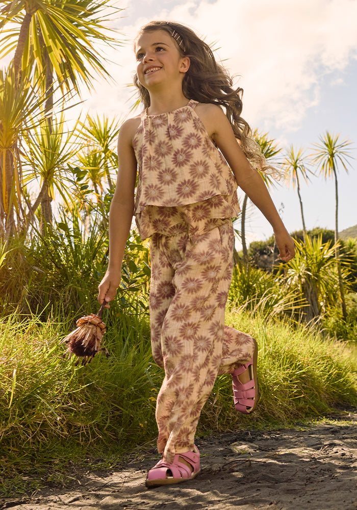 Image of a girl wearing a flowery outfit while walking outside wearing pink closed-toe Bobux sandals